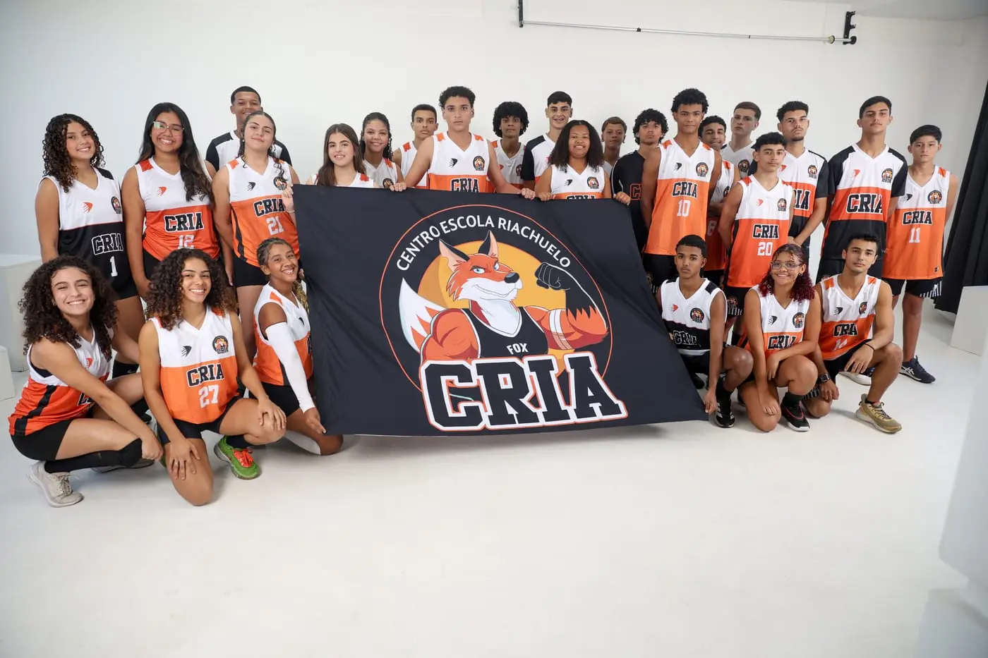 Atletas dos Crias reunidos com o uniforme laranja atrás da bandeira CRIA