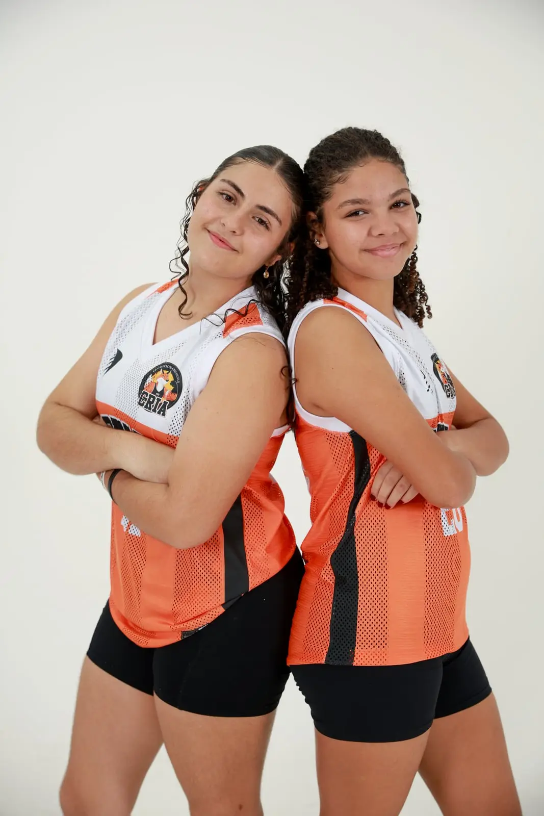 Duas atletas dos Crias de costas uma para a outra, com a camisa laranja