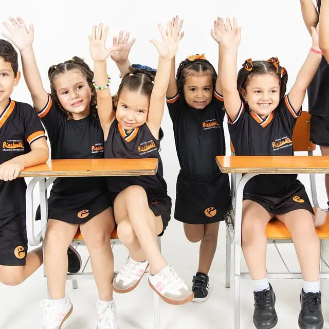 Turminha da Educação Infantil nas carteiras, de braços para cima