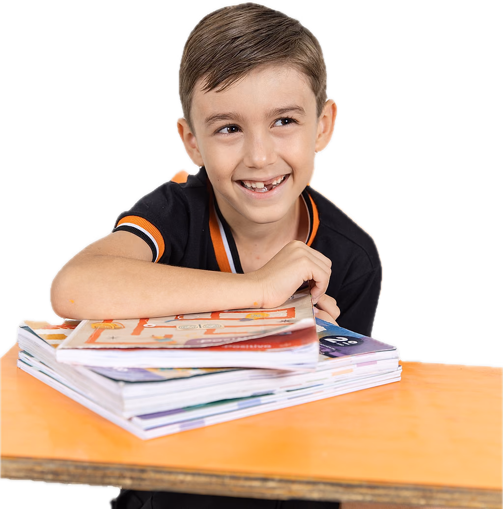 Aluno do Riachuelo sorrindo, debruçado na carteira com os livros