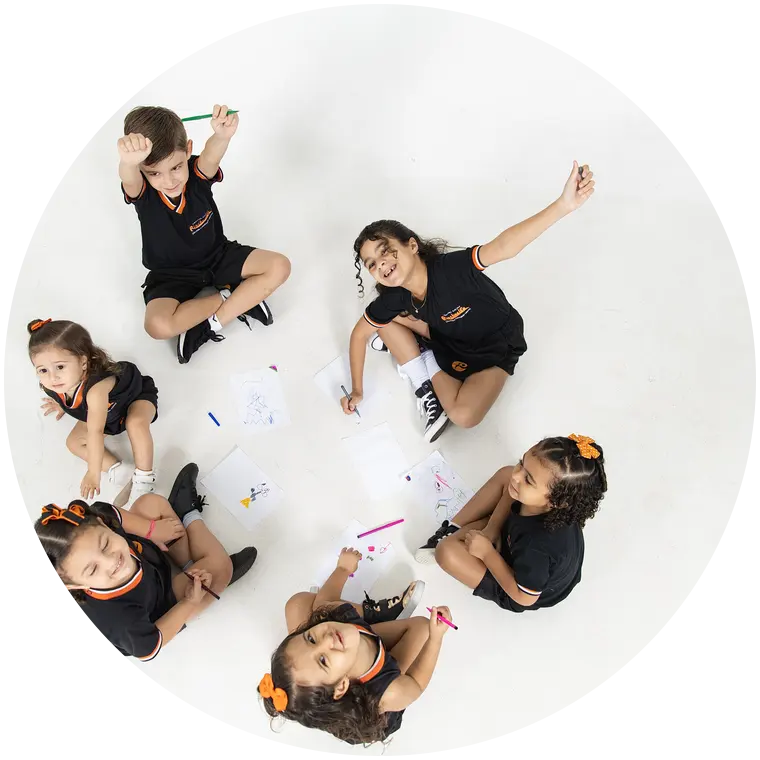 Roda de crianças no chão, criando desenhos juntas e sorrindo para cima